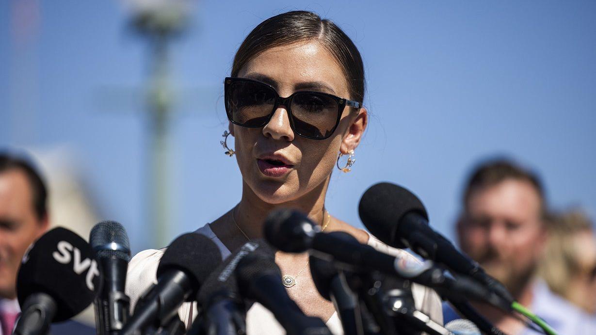 Mulher falando ao ar livre, cercada por microfones e pessoas