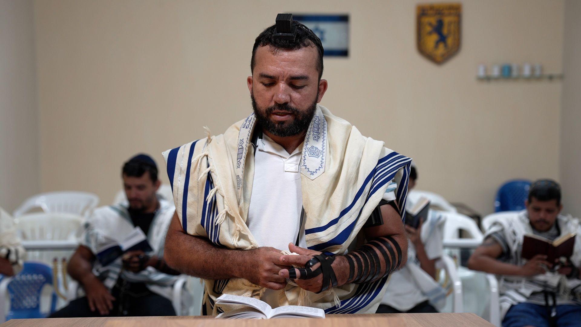 Homem com xale e outros itens religiosos judaicos reza em sinagoga.