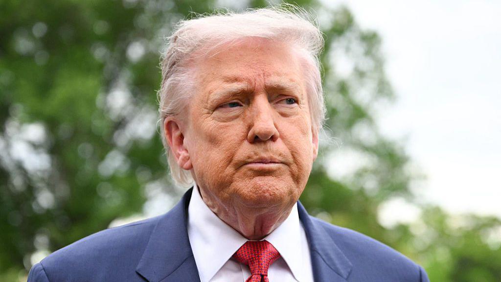 Donald Trump con una expresión seria, vistiendo un traje azul marino y una corbata roja.