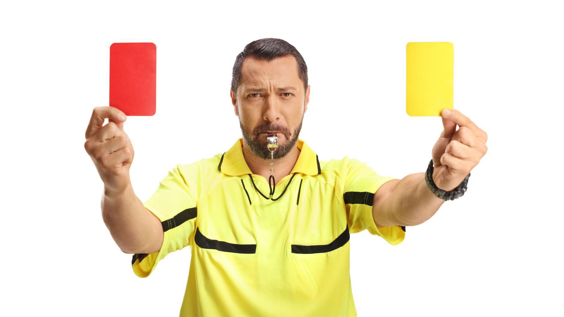 Referí con un silbato en la boca y una tarjeta roja y una amarilla en cada mano.