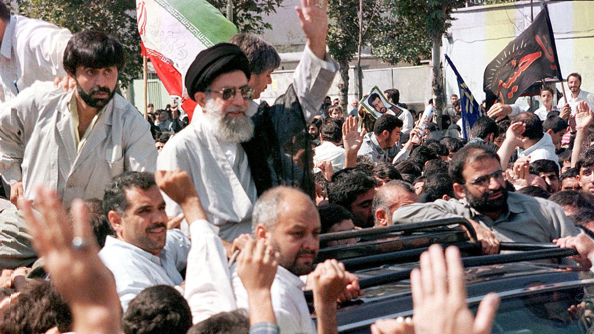 Khamenei waves to a crowd by standing up in an open-topped car on 18 September 1998 in Tehran. Several thousand Iranians took to the streets to express anger at the Taliban in Afghanistan ahead of a funeral for a group of Iranians killed by the militant group.