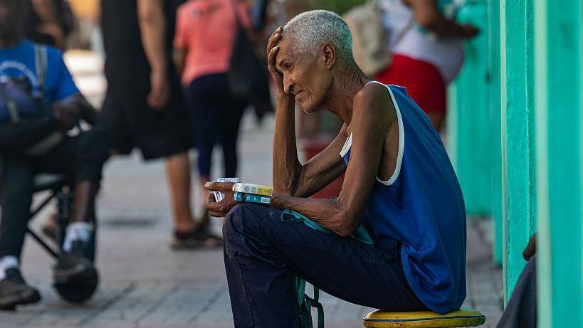 Hombre sentado en una calle en Cuba vende paquetes de cigarrillos. 