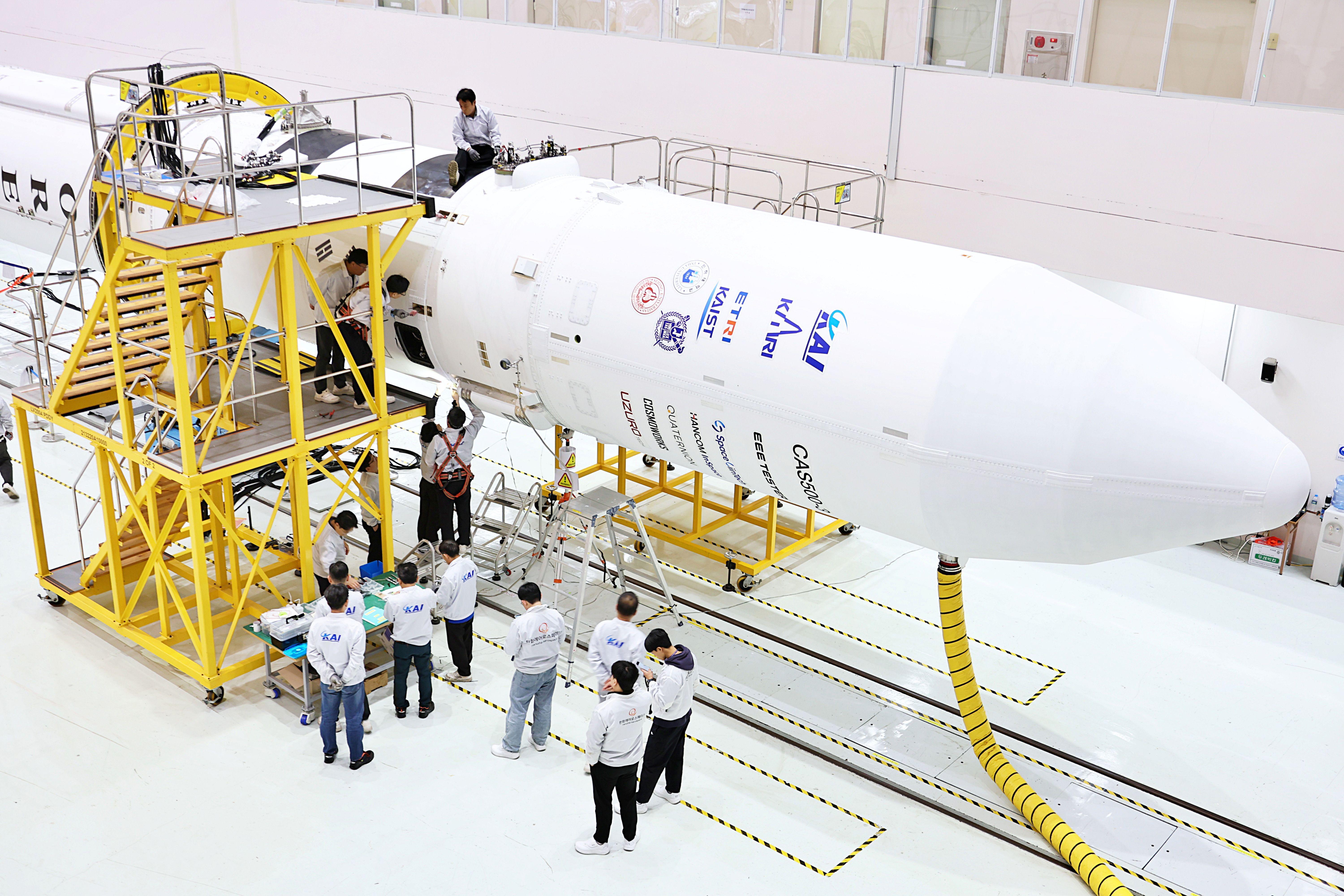 나로우주센터 조립동에서 연구진들이 누리호 4차 발사 총조립을 수행하고 있다. 가로로 누운 로켓 주위로 연구진들이 모여서 논의를 하고 있다