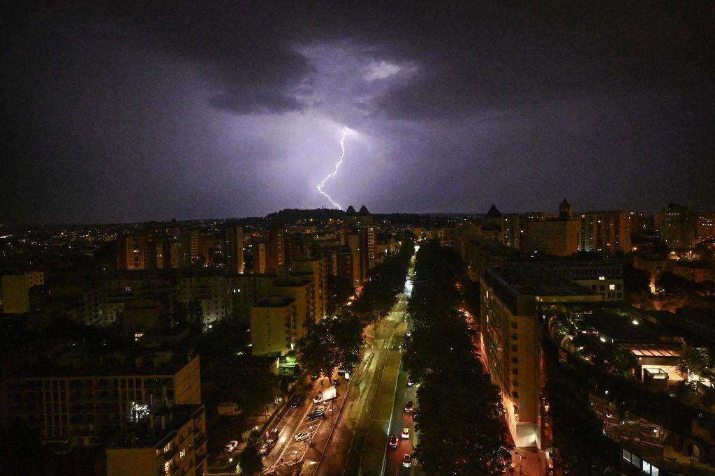 صاعقة برق في منطقة الأعمال التجارية لا ديفونس خارج باريس، الصورة التقطت ليلاً حيث مجموعة مبانٍ سكنية وسيارات وسماء سوداء مليئة بالغيوم وتظهر وسطها صاعقة برق.