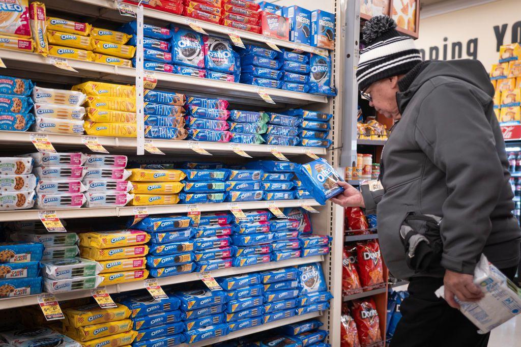 Un hombre mira un paquete de galletas ultraprocesadas frente a un estante lleno de esos productos