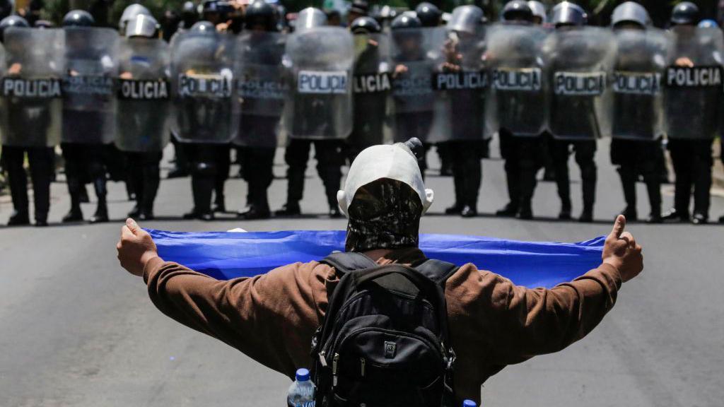 Un manifestante enmascarado muestra una bandera nicaragüense a un grupo de policías antidisturbios el 16 de septiembre de 2018.