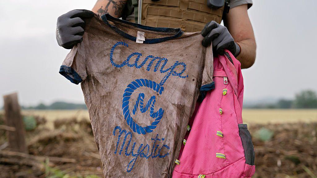 Un rescatista con una camiseta y una mochila de una niña que estaba en el campamento Mystic.