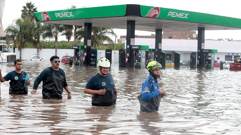 Personas caminan en medio del agua que les cubre la mitad del cuerpo en Jalisco.