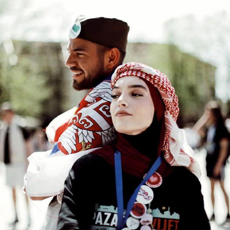 Devojka sa hidžabom na glavi i muškarac sa srpskom šajkačom na glavi