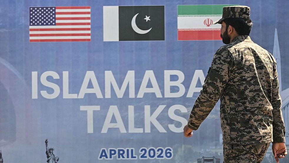 Un soldado pakistaní vestido con uniforme de camuflaje pasa junto a una valla publicitaria sobre las conversaciones de paz entre Estados Unidos e Irán en Islamabad.