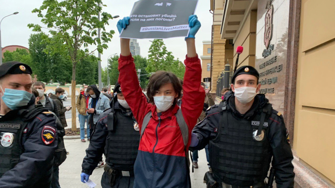 一名年輕男子手持寫有「阻止那些戴肩章的殺手」的標語牌，警察押送他朝鏡頭方向走來