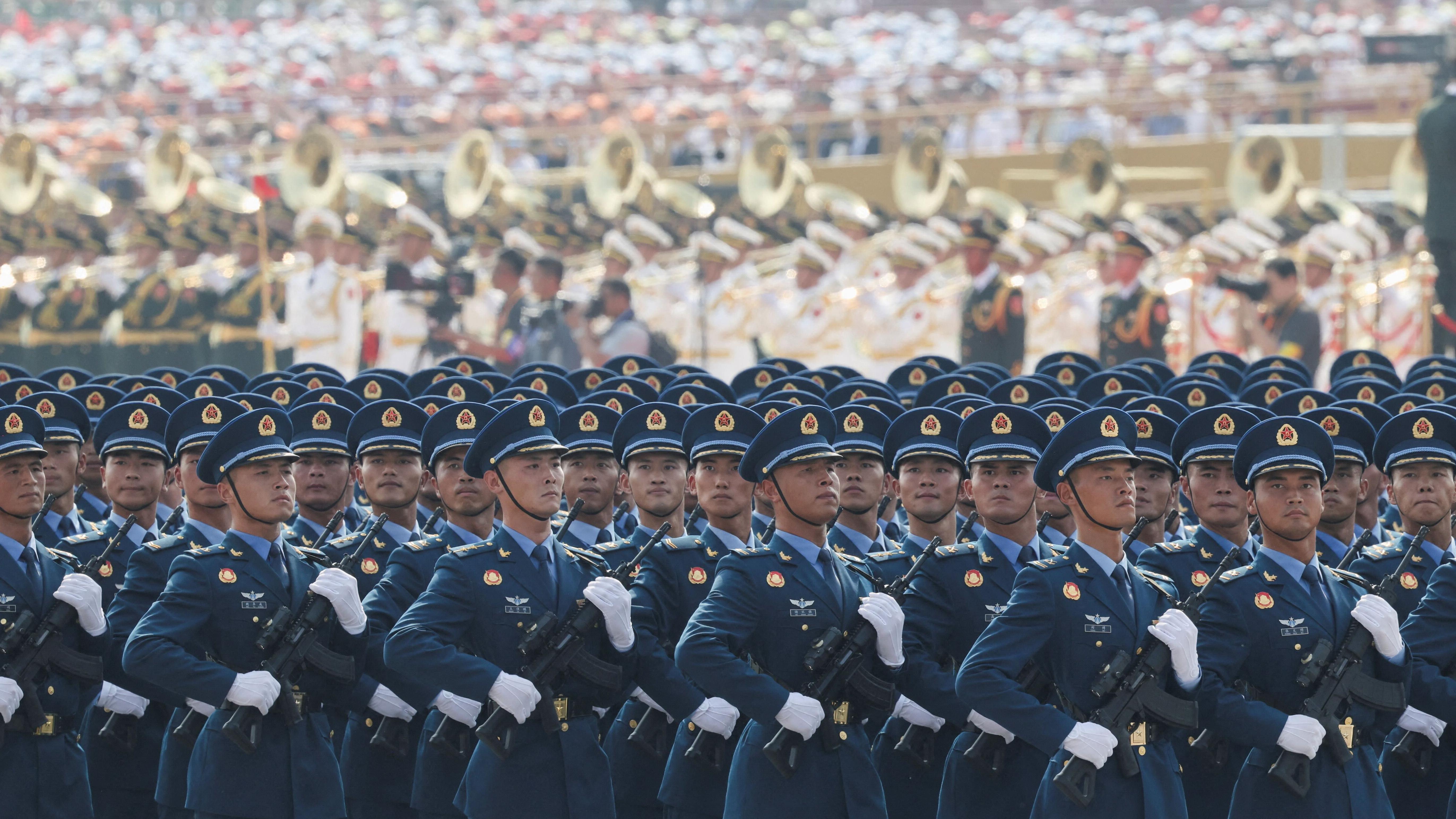 Soldados chinos con uniforme azul desfilan armados en formación.