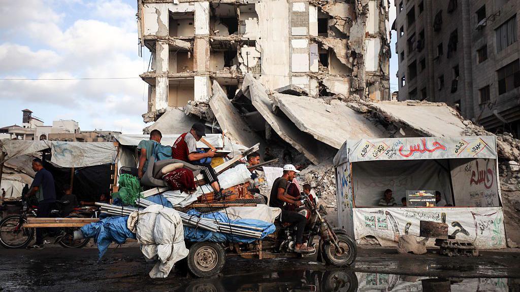 نازحون من مدينة غزة إلى الجنوب مع أغراضهم فوق عربة صغيرة تجرها دراجة نارية.