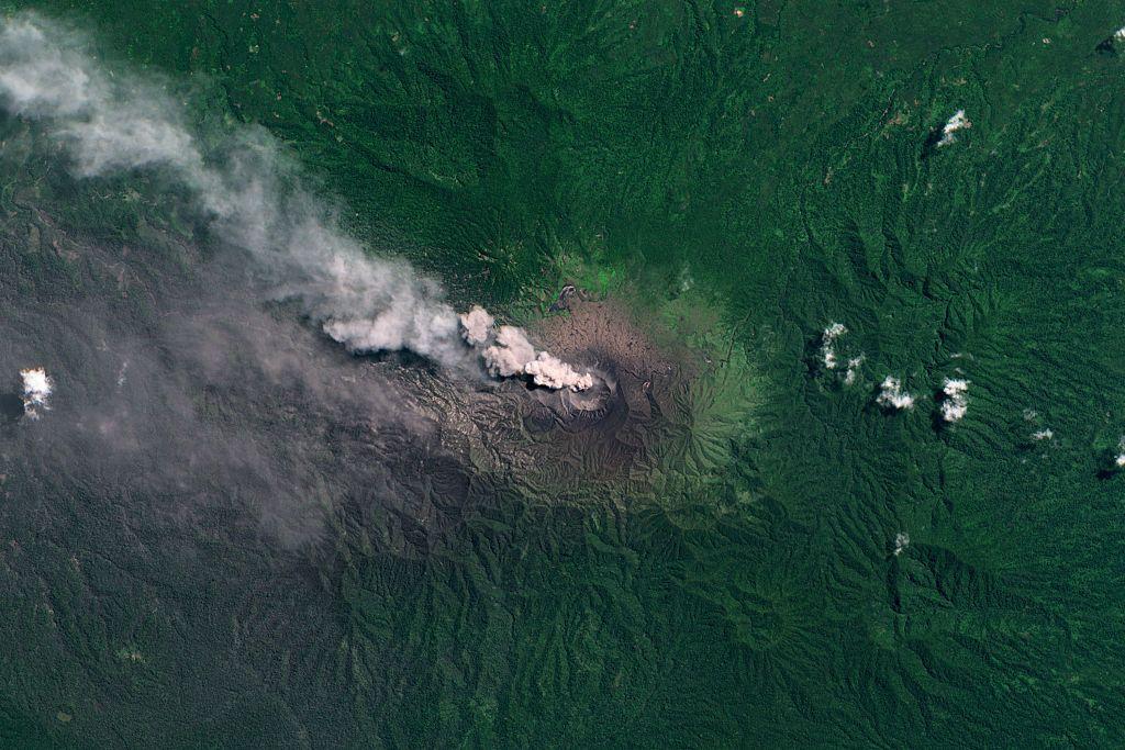 Imagem de sat&eacute;lite do Monte Dukono mostrando nuvens de fuma&ccedil;a saindo da cratera do vulc&atilde;o, cercadas por uma densa vegeta&ccedil;&atilde;o verde