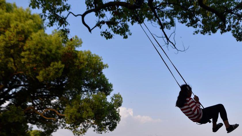 A close-up image of a young girl on a swing in a park 