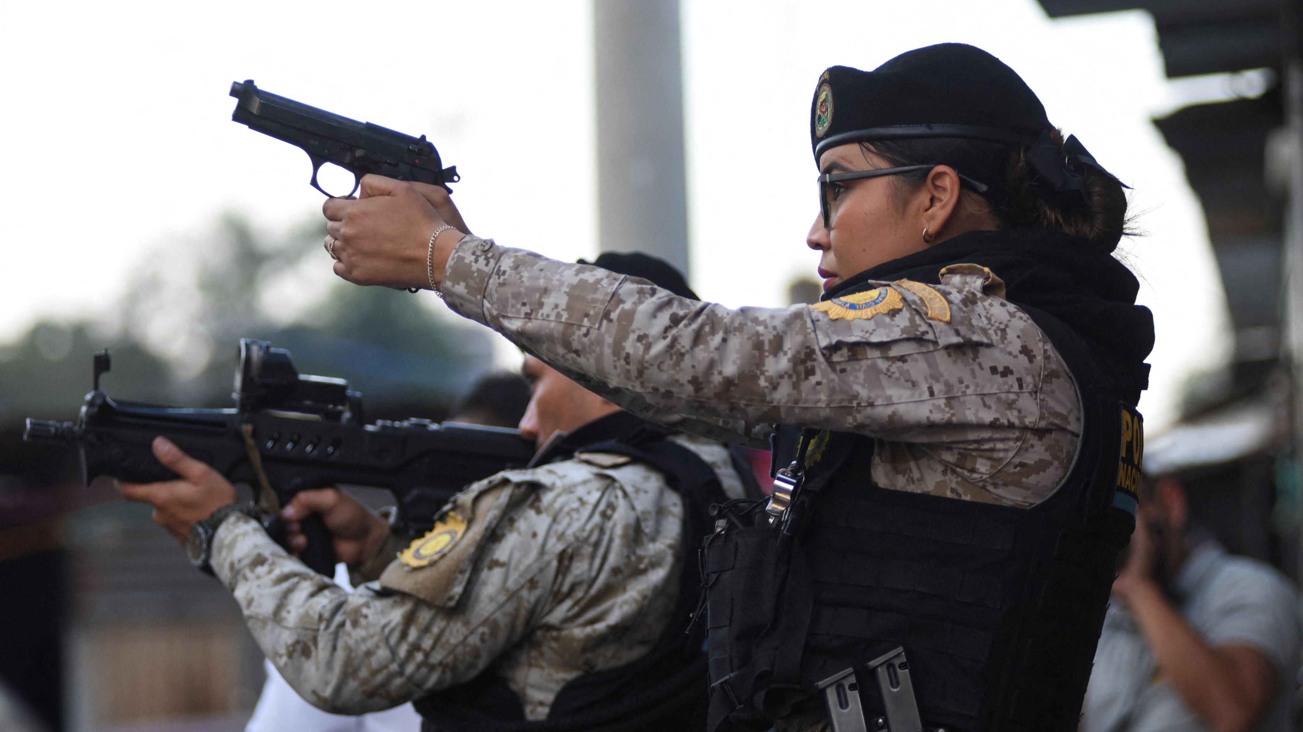 Una funcionaria de policía apunta con su arma. A su lado, otro agente, apunta con un fusil. 