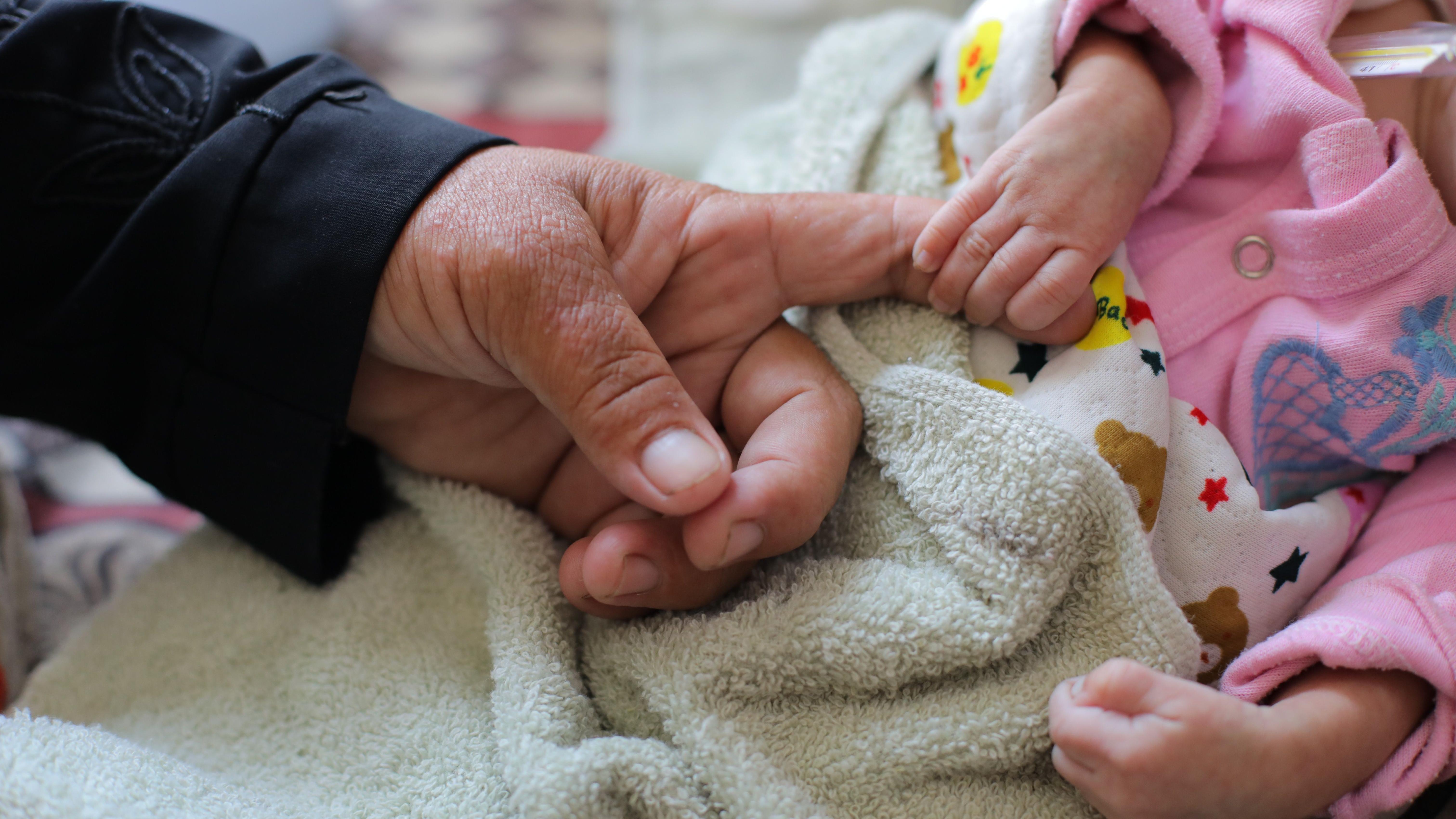 صورة تظهر يد طفلة رضيعة تمسك بأصبع سيدة كبيرة توثق معاناة أطفال من سوء تغذية حاد. ويتلقون العلاج في مستشفى شهداء الأقصى بدير البلح، قطاع غزة، في 20 أغسطس/آب 2025. 