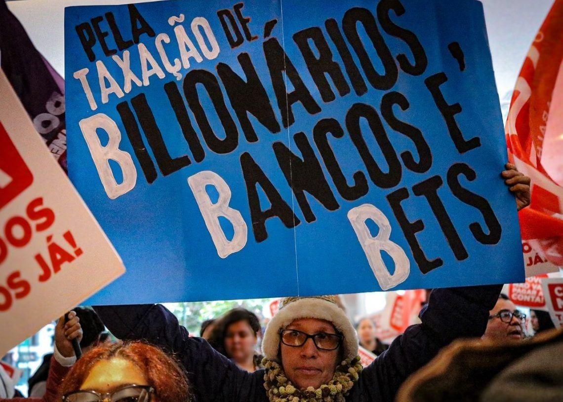 Manifestante durante protesto na sede do banco Itaú BBA, em São Paulo, com um cartaz onde se lê: 