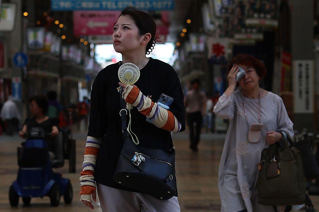 Una mujer en Japón con un ventilador portátil, mientras otra detrás se seca el sudor de la frente con un pañuelo.
