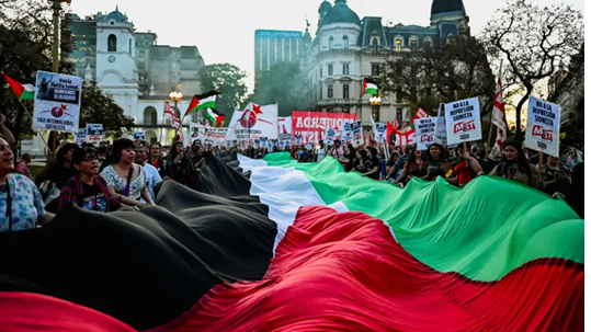 إسرائيل تواجه إدانات دولية عقب اعتراضها "أسطول الصمود العالمي" المتجه لغزة 3 مؤيدون للفلسطينيين يحملون علماً فلسطينياً ضخماً خلال مظاهرة تضامناً مع "أسطول الصمود العالمي" وغزة، في بوينس آيرس في الأرجنتين