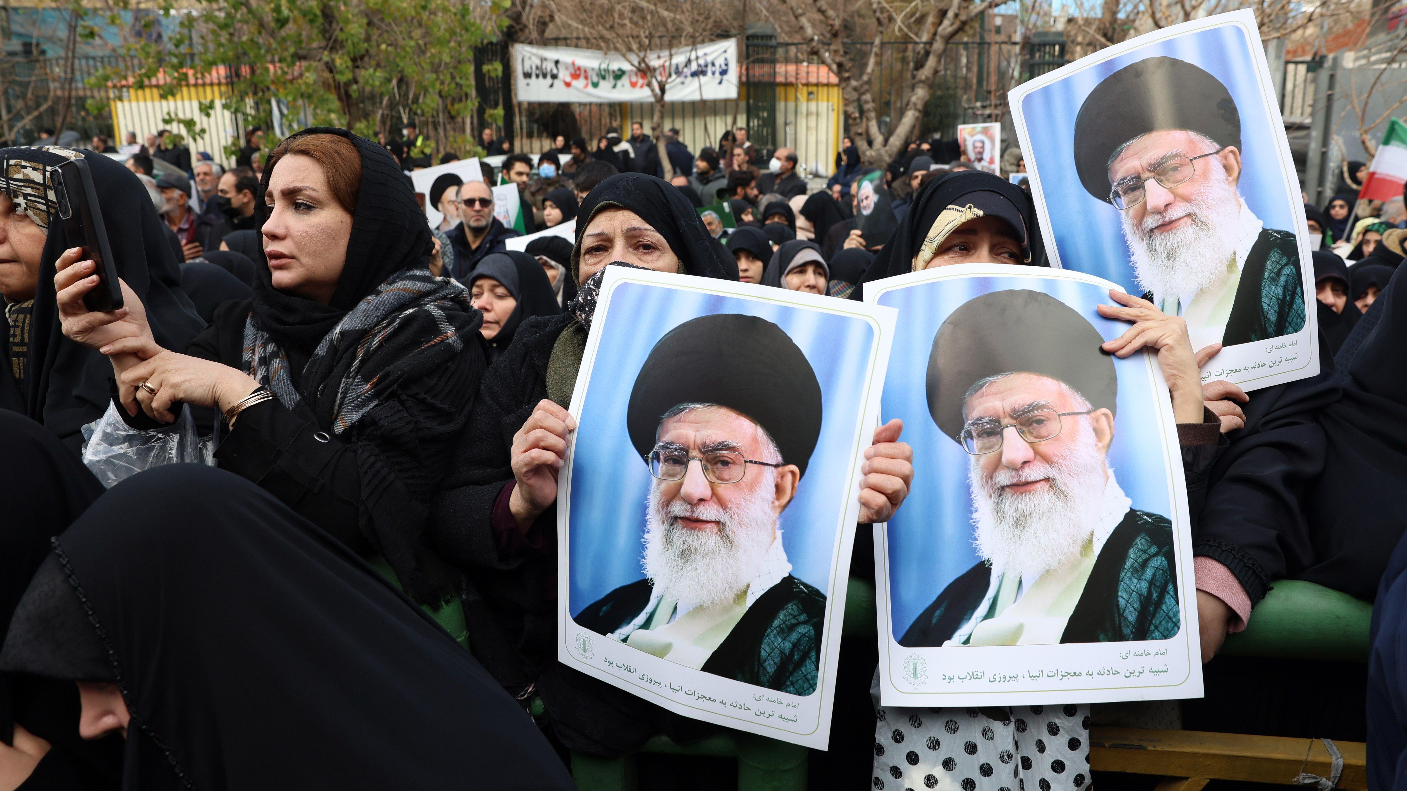Woman dressed in black robes gather in an outdoor public area on 14 January 2026. Three of them are holding posters of Khamenei.