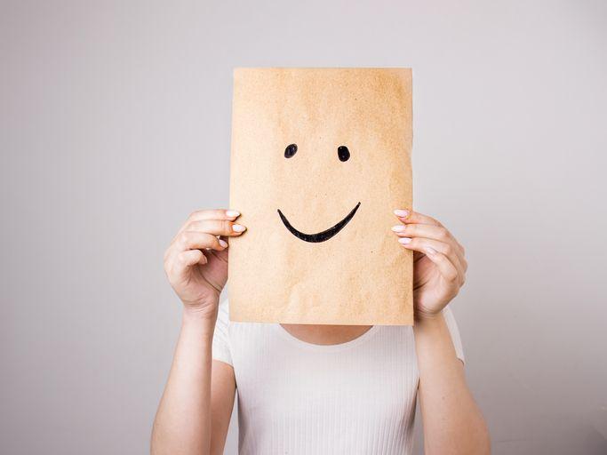 Mulher cobrindo o rosto com papel com um sorriso desenhado