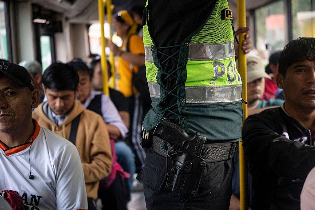 Un policía viaja con su arma reglamentaria en la cintura junto a varias personas sentadas en un autobús en las afueras de Lima, Perú, en abril de 2026