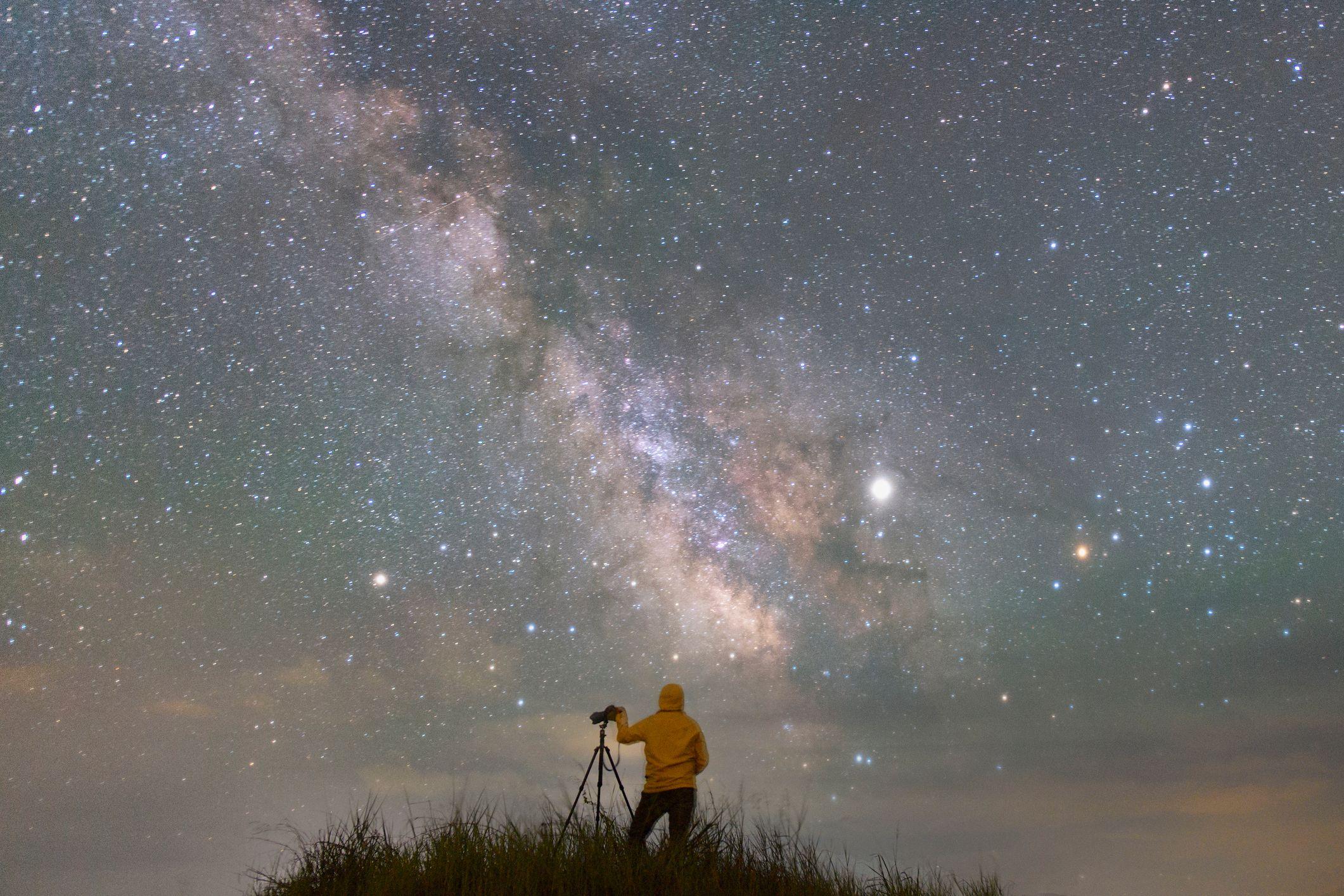 Pessoa observa o céu estrelado ao lado de um telescópio