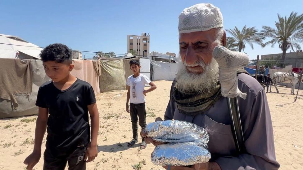 Un hombre mayor con muletas sostiene dos paquetes con comida