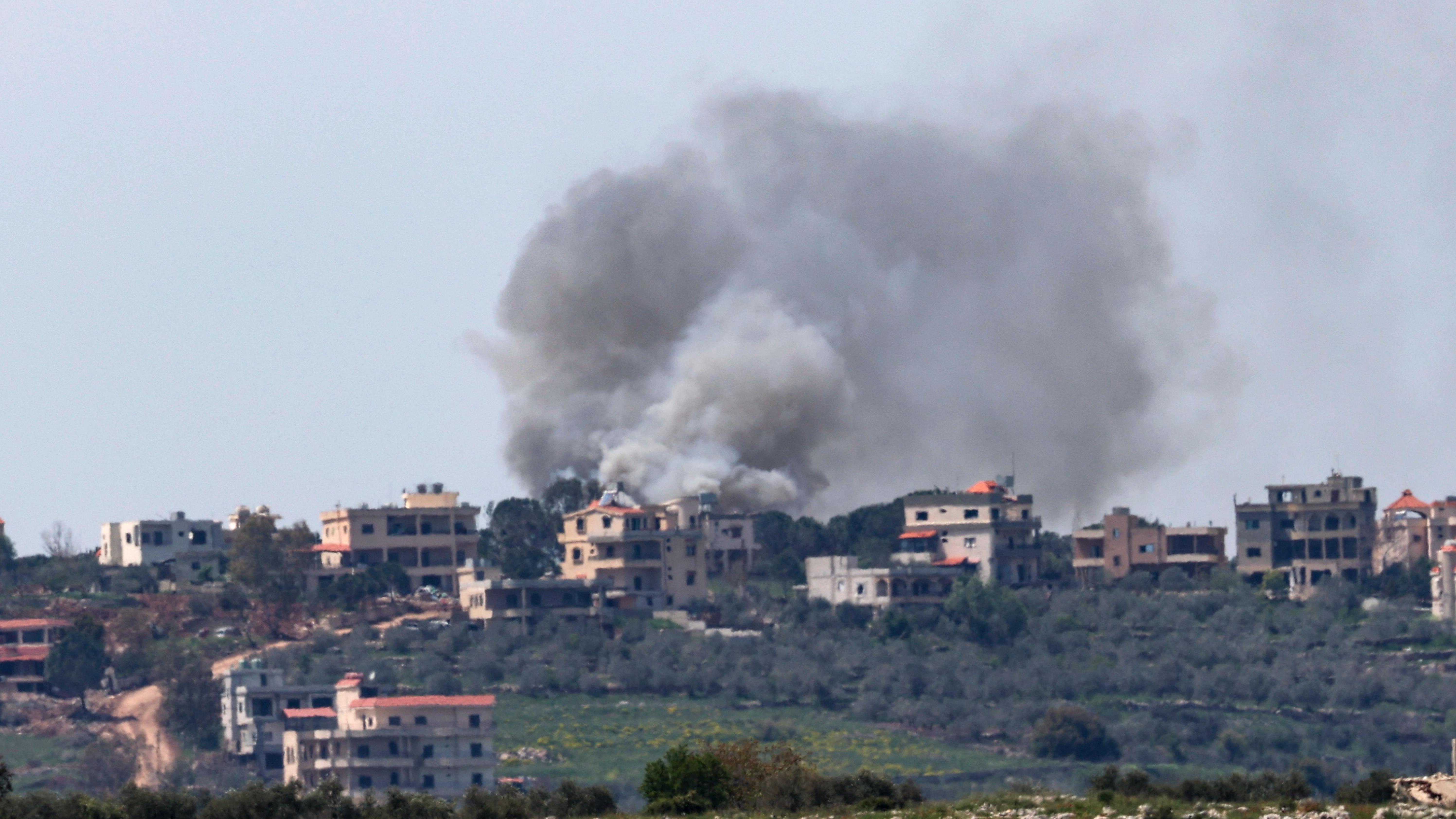 تلة تظهر فيها عدة منازل ودخان قصف وأشجار زيتون - صورة من بلدة بنت جبيل