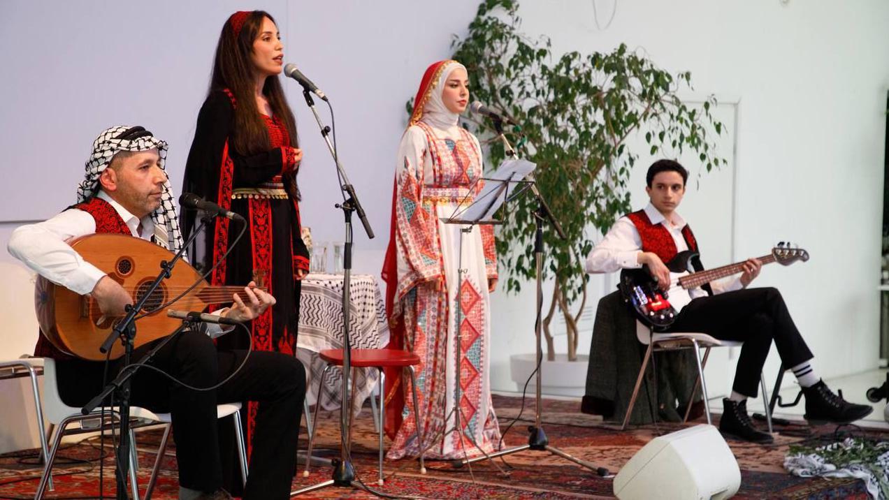 خلود إبراهيم، ترتدي لباساً تقليدياً، وتغني مع كورال "ناي" في حفلة موسيقية إلى جانب عازفين.