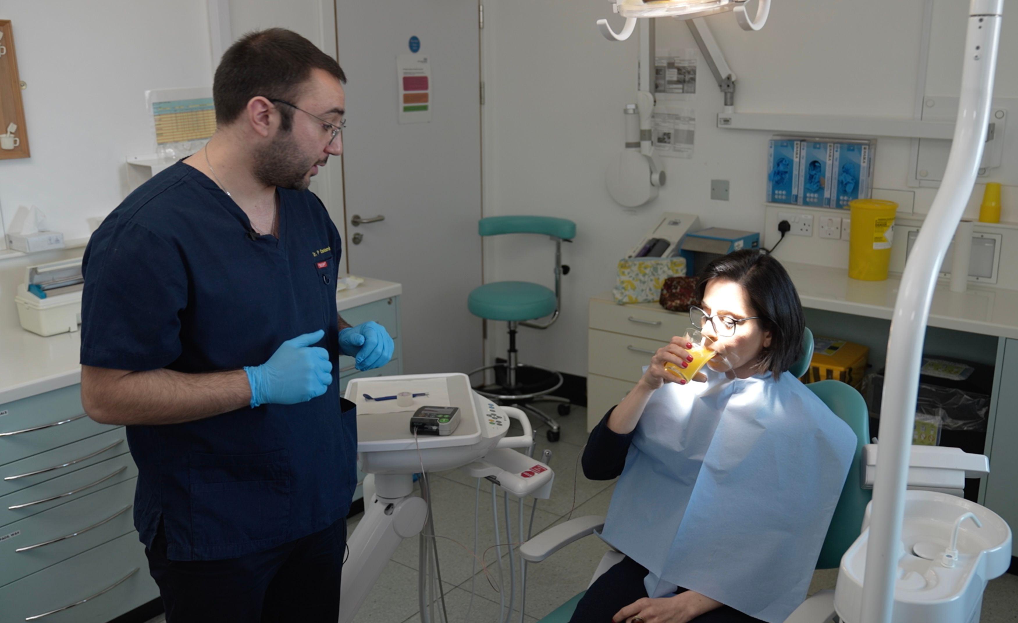 Dr Charalambous uses a pH meter to measure the acidity in BBC reporter's mouth while she drinks orange juice.