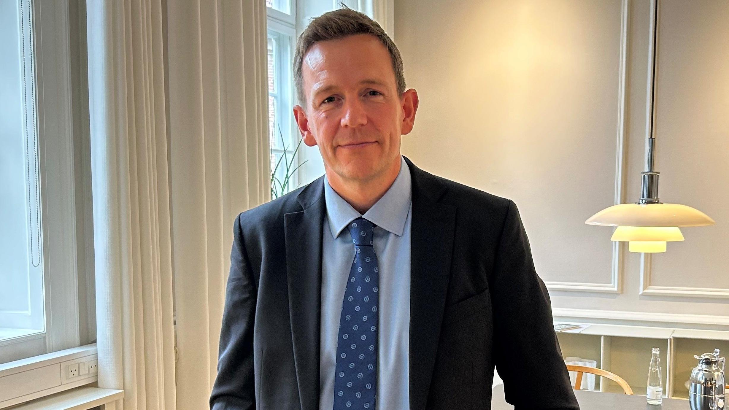 留著金色短髮，身穿西裝、打著領帶的拉斯穆斯·斯托克倫在他辦公室的窗邊。