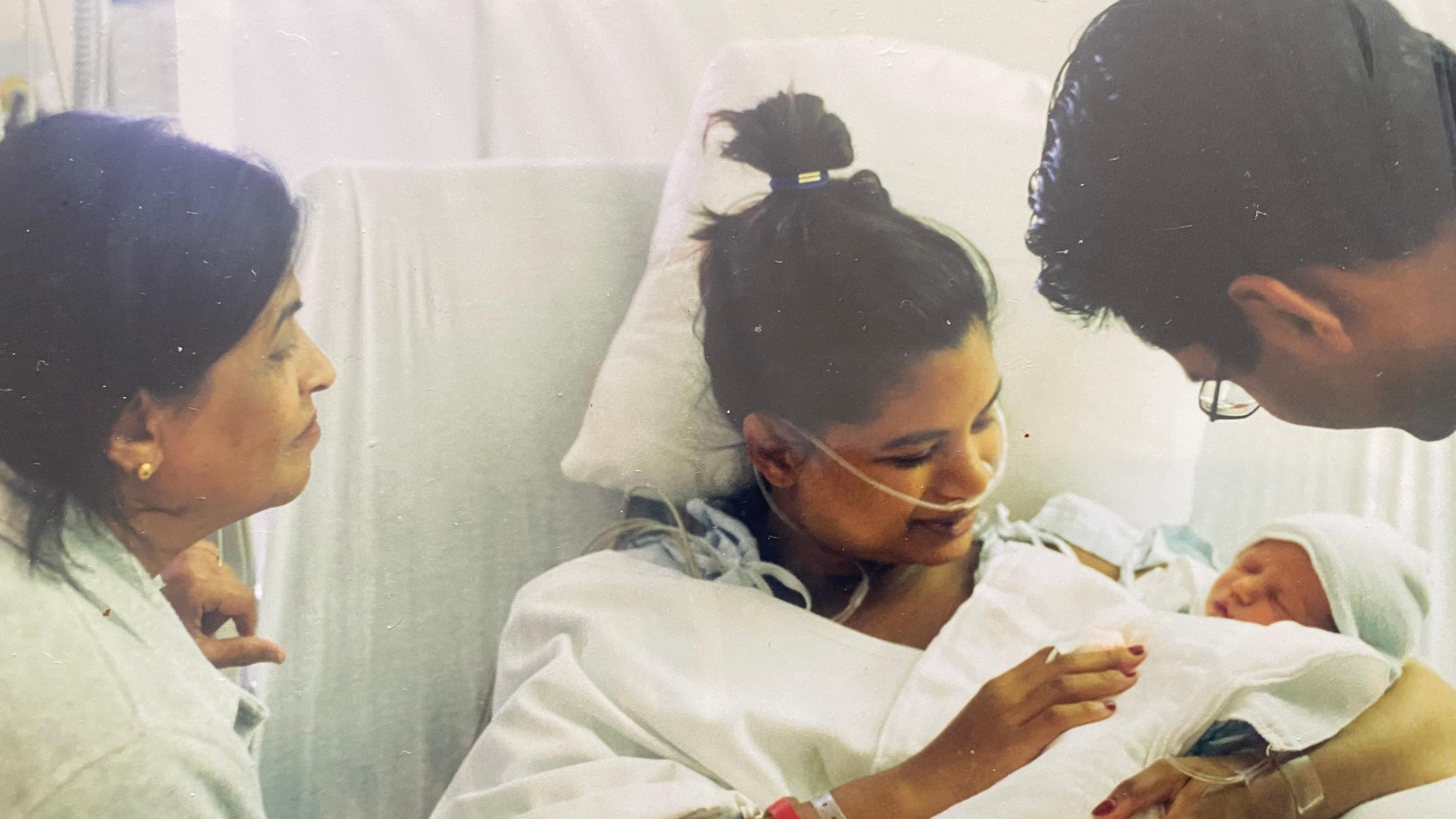 Con una almohada detrás de la cabeza y un montón de cables y tubos conectados a ella, Samina Ali está acostada  en una cama de hospital, mirando a su hijo pequeño, Ishmael, en brazos, junto a su madre y su hermano menor.
