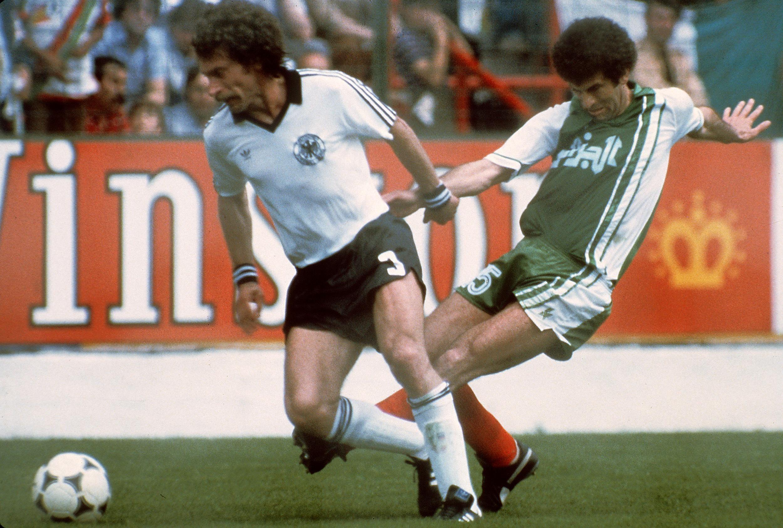 لاعب ألمانيا الغربية بول برايتنر (يسار) يحاول السيطرة على الكرة تحت ضغط من الجزائري مصطفى دحلب خلال مباراة في الدور الأول من كأس العالم في 16 يونيو/حزيران 1982 في خيخون.