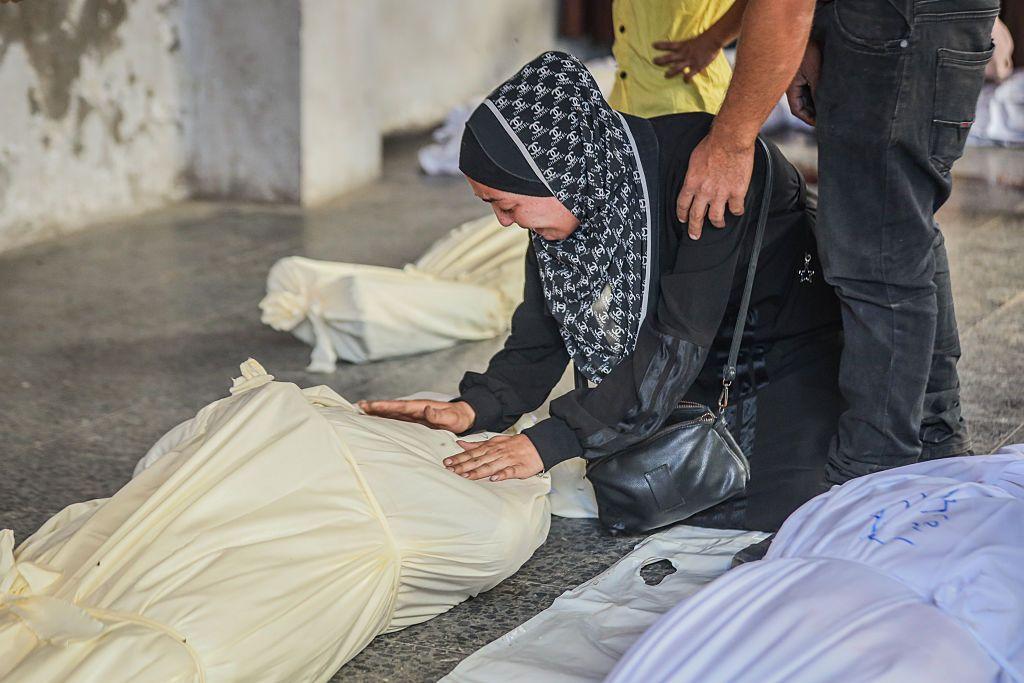 سيدة فلسطينية تنحني أمام جثة أحد أقاربها بجوار جثث أخرى قبل تشييعها