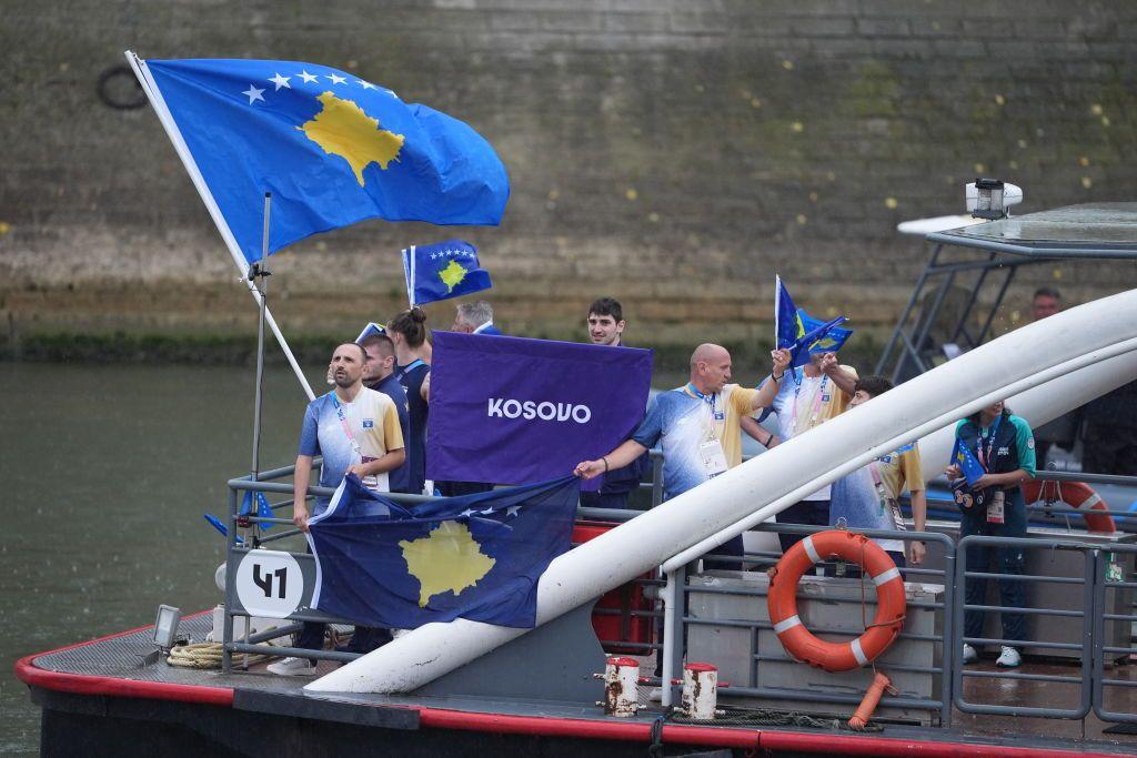 Barco no rio mostra atletas sorrindo e bandeiras de Kosovo