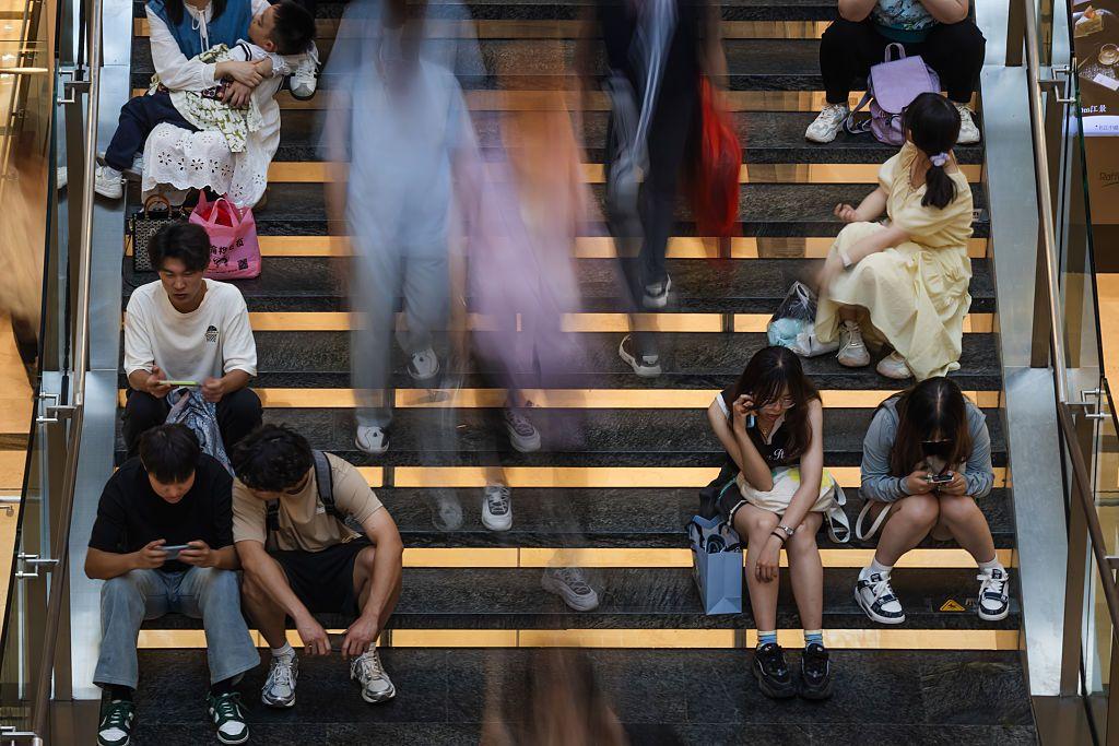 يجلس الناس على درج ليستريحوا بينما يمرّ آخرون بجانبهم بسرعة، في لقطة ذات تأثير ضبابي للحركة داخل مركز «رافلز سيتي تشونغتشينغ» في ١ مايو/ أيار ٢٠٢٥ في تشونغتشينغ، الصين.