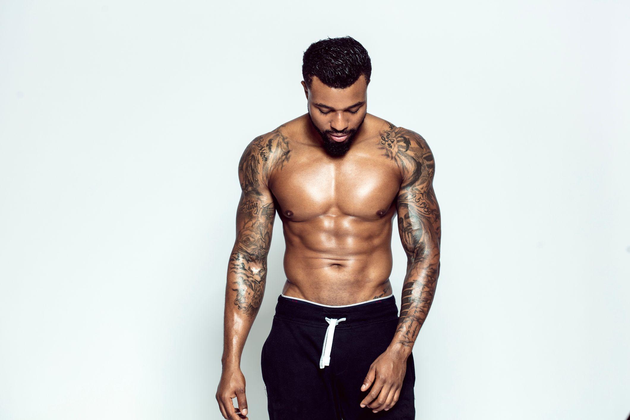 Homem com os bra&ccedil;os tatuados, sem camisa, olhando para baixo
