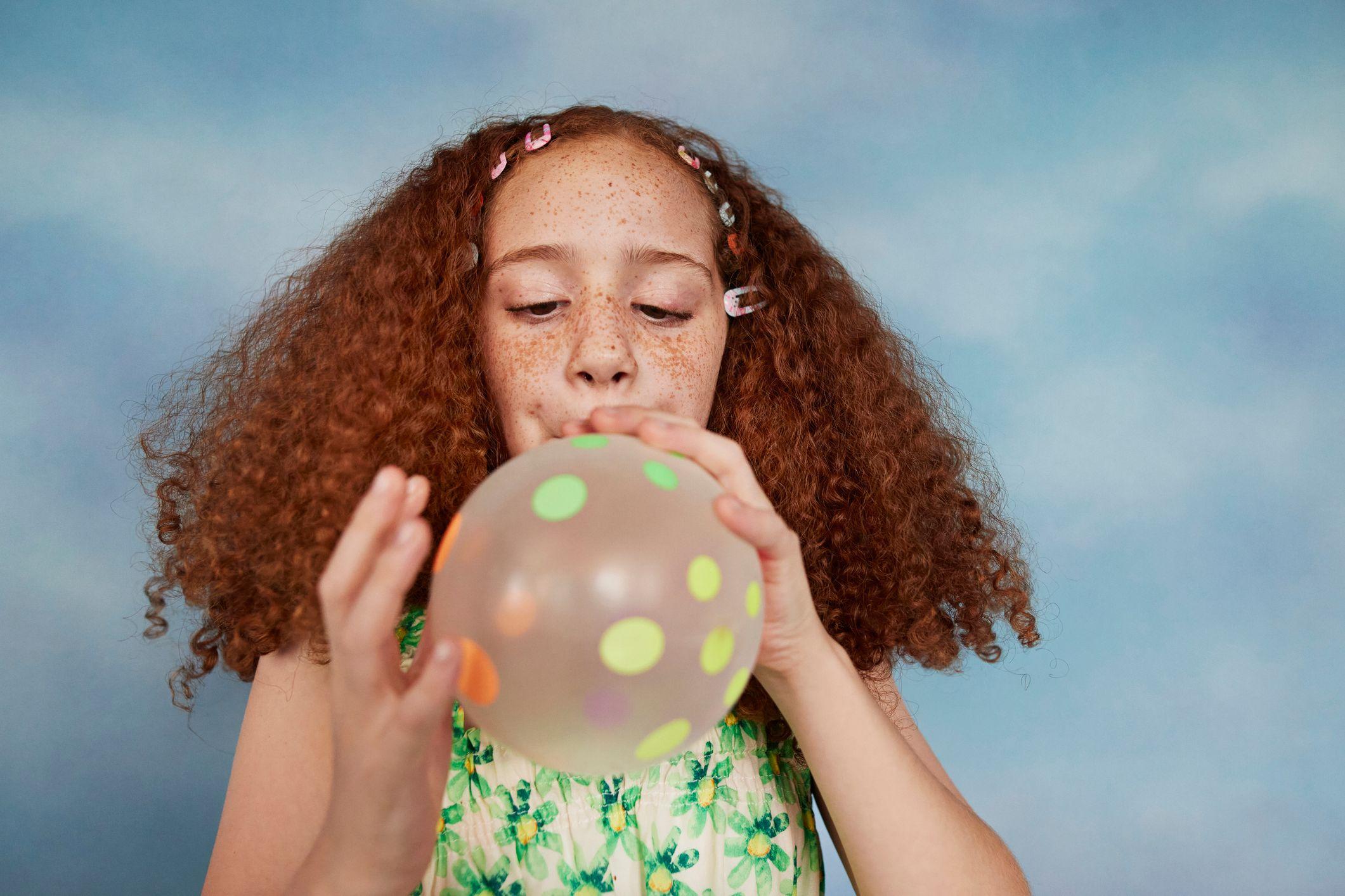 Una niña infla un globo con puntos en su superficie.