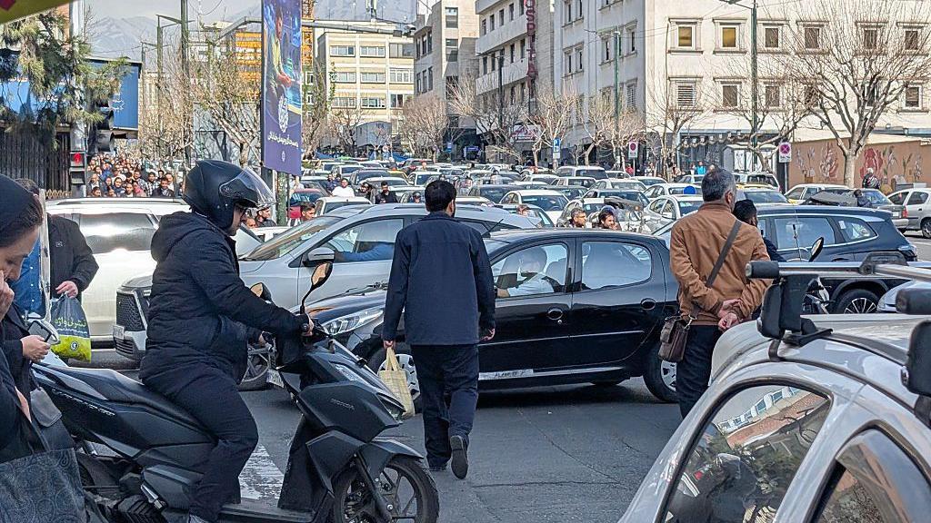 Iraníes intentan despejar una calle en medio del denso tráfico en Teherán,