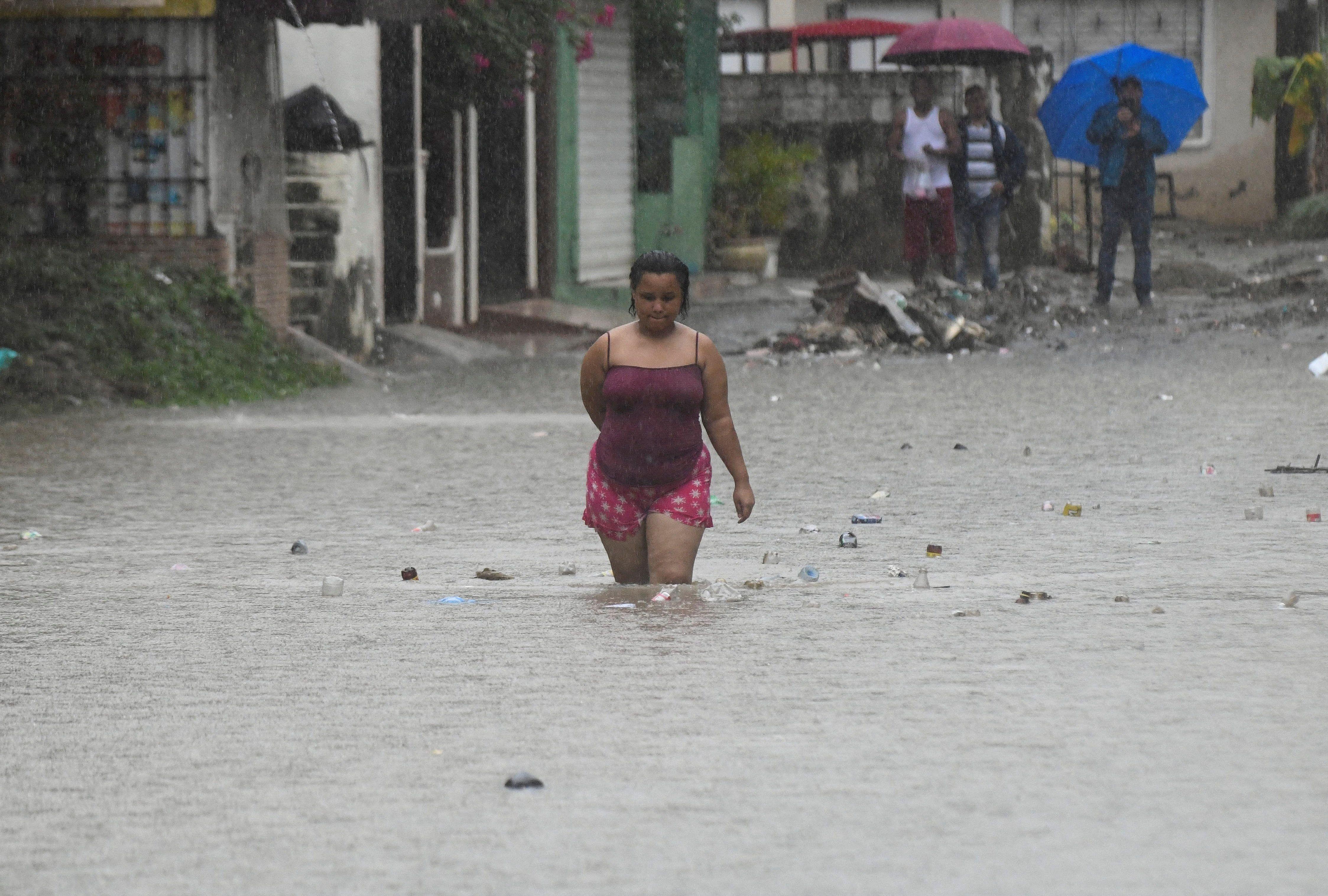 Una mujer con el agua hasta las rodillas camina en una calle inundada en República Dominicana