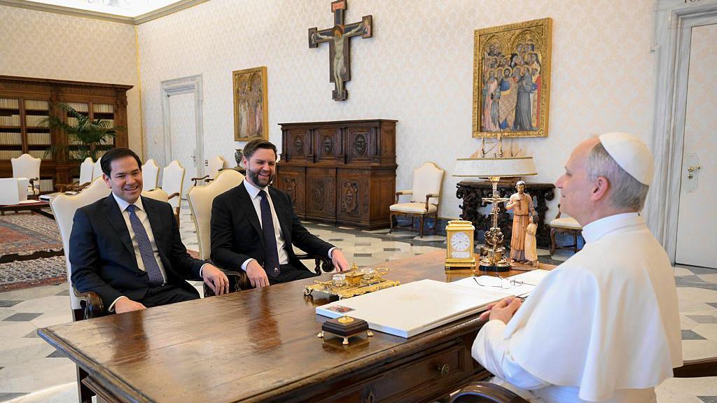 El papa León XIV se reúne con el vicepresidente estadounidense JD Vance y el secretario de Estado estadounidense Marco Rubio el 19 de mayo de 2025 en la Ciudad del Vaticano. Ambos están sentados frente a él, separados por el escritorio del papa. El papa viste su tradicional túnica blanca, mientras que Rubio y Vance llevan traje.