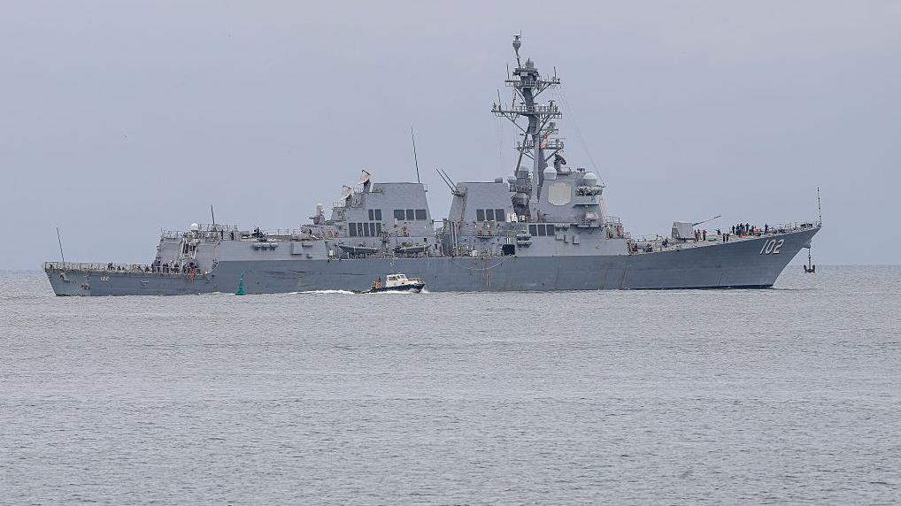 En un mar tranquilo navega un barco de guerra de color gris con el número 102 escrito es letras blancas en su proa.