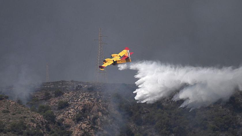 Un hidroavión de color amarillo ayuda en las tareas de extinción del fuego arrojando agua desde el aire. 