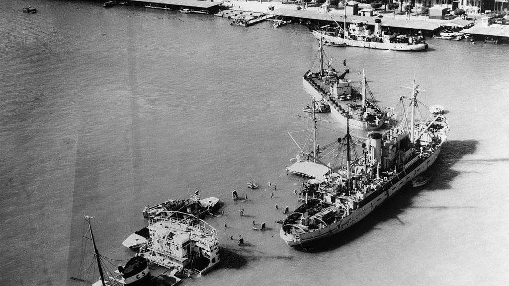 أزمة السويس. من الجو، تظهر سفن الحصار التي غرقت عند مدخل قناة السويس في بورسعيد. في أقصى اليمين، إحدى سفن الإنقاذ التي بدأت بالفعل أعمال تنظيف القناة.