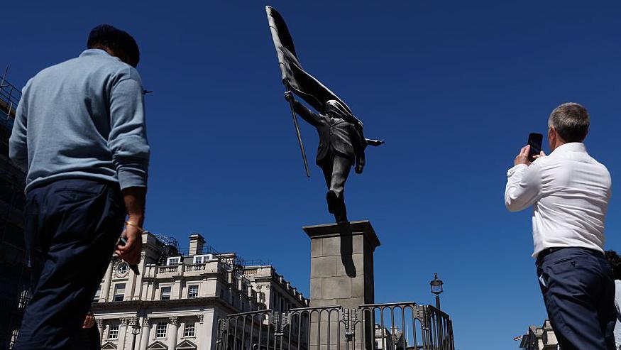 Personas tomando imágenes de la estatua con sus teléfonos celulares. 