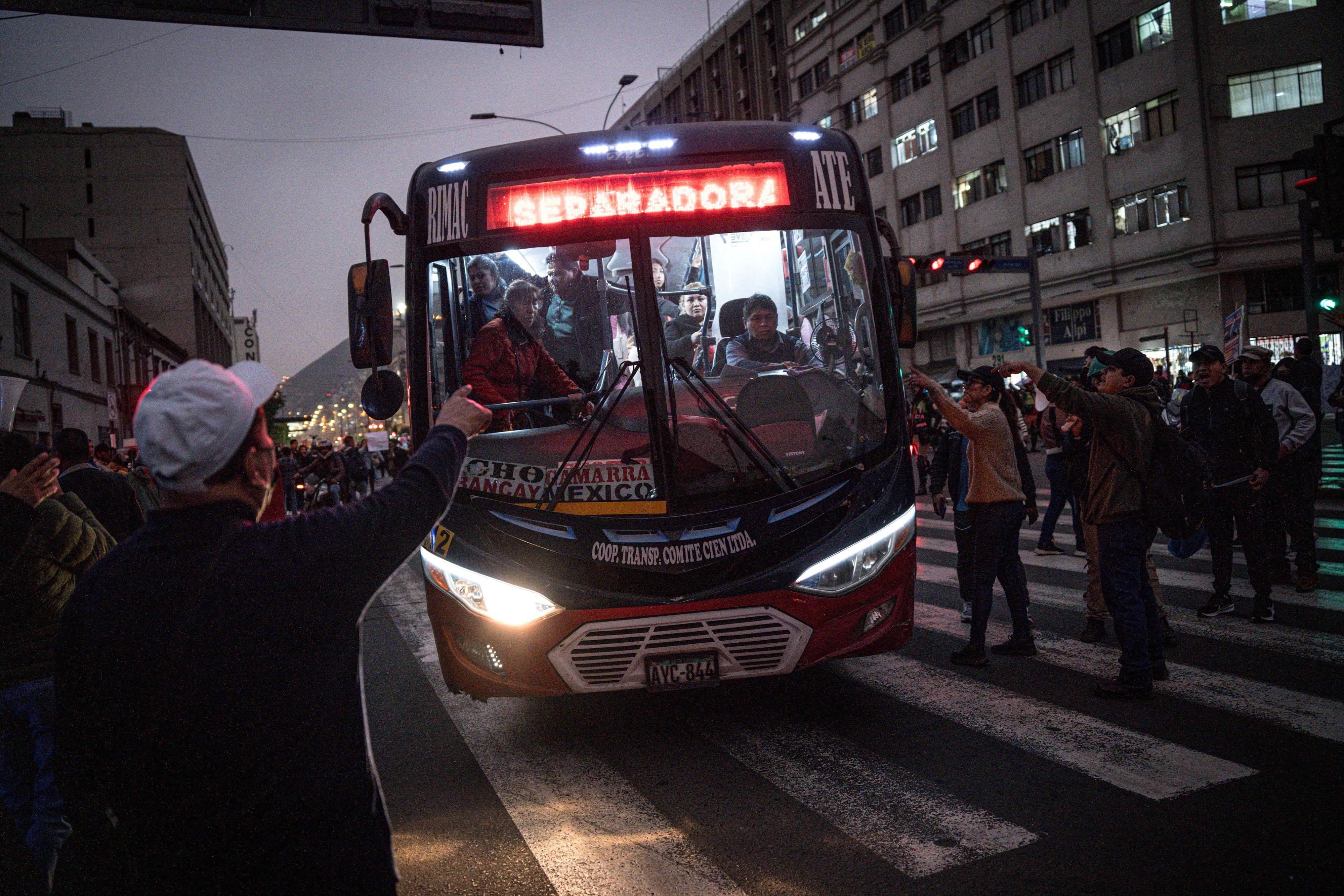 Un autobús maniobra en medio de una grupo de personas que gesticulan hacia él en el centro de Lima. 