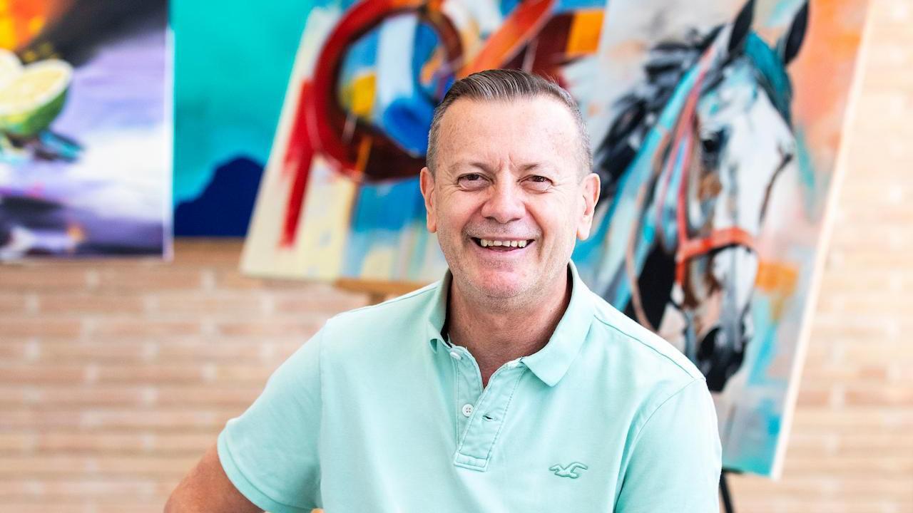 Gustavo Zuluaga posa sentado con varias pinturas en el fondo.