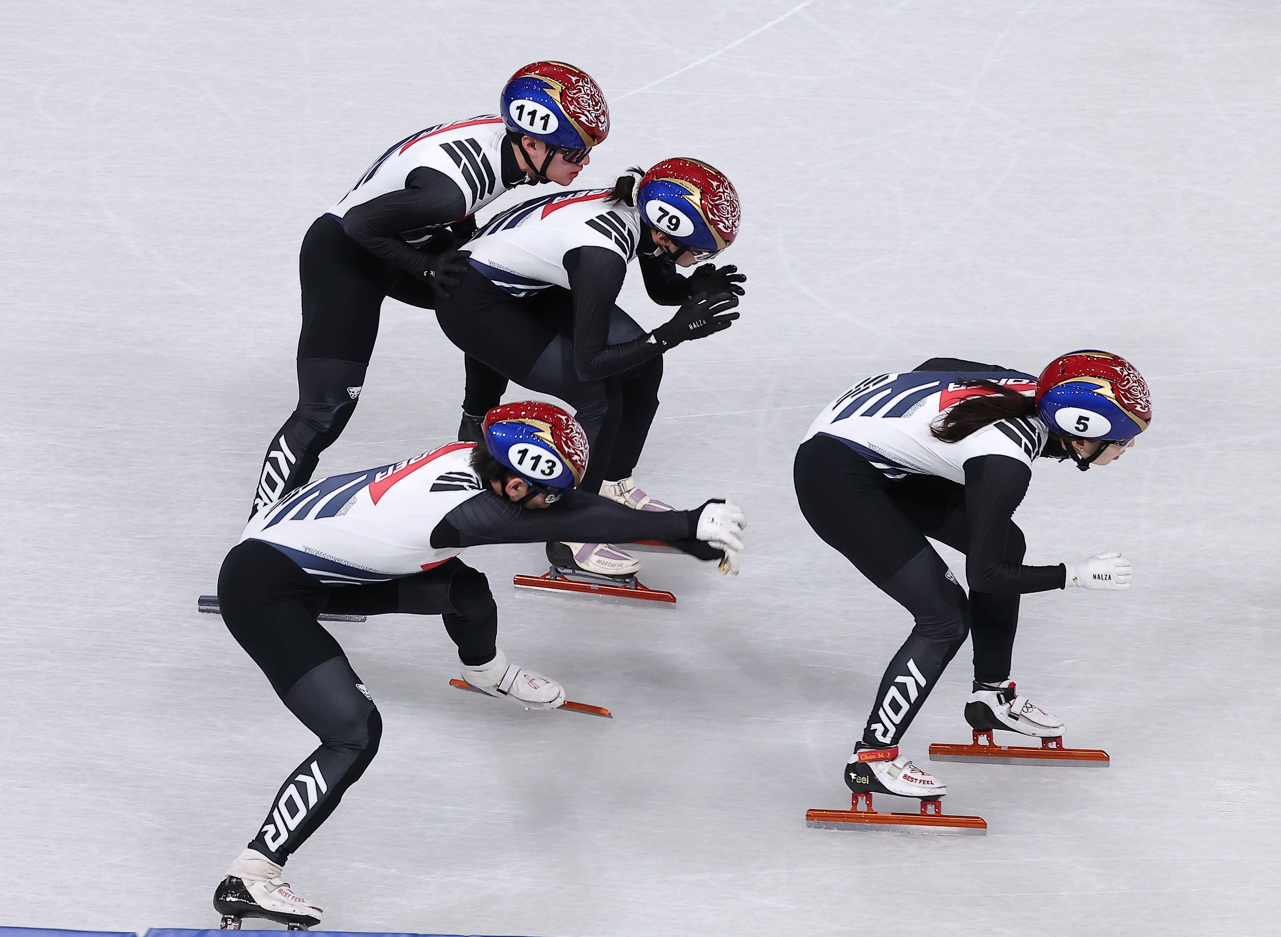 이탈리아 밀라노 아이스스케이팅 아레나에서 한국 쇼트트랙 여자 선수들이 국가대표 선수복을 입고 계주 훈련을 하고 있다. 네 명의 선수가 차례로 빙판을 돌며 손으로 등을 밀어주는 교대 동작을 반복하고 있다.
